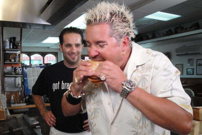 Guy Fieri eats a sandwich on the set of a restaurant for Diners, Drive-Ins and Dives