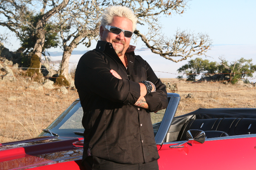 Guy Fieri poses in front of a red convertible car