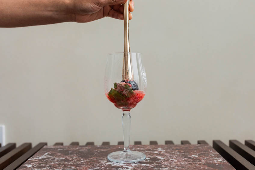 Strawberries and mint being muddled in a wine glass