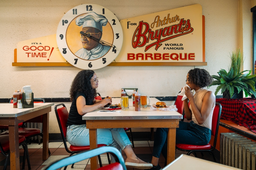 Two women eating at a table under the Arthur Bryant's sign at the famous Kansas City barbecue restaurant