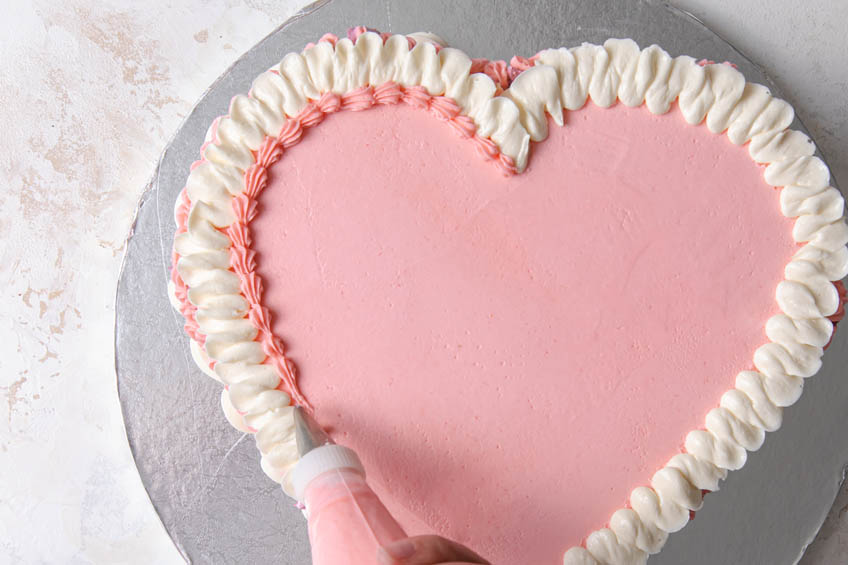 A heart shaped cake trimmed with iced ruffles on top