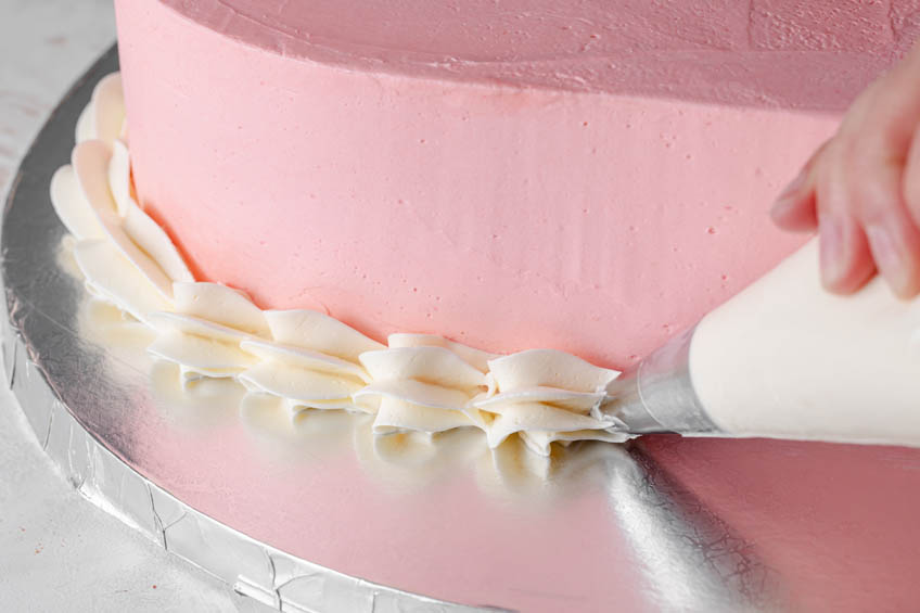 A heart-shaped cake being frosted with a white shell border