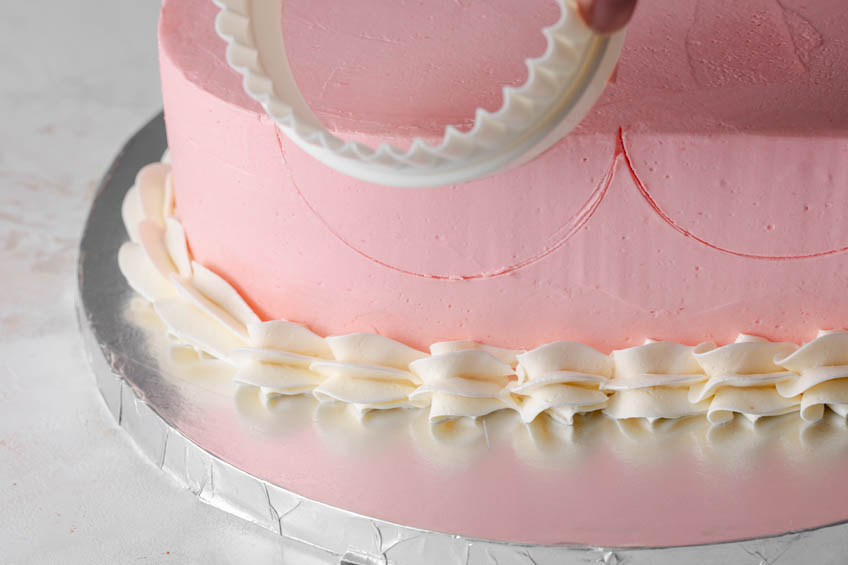 A cookie cutter being used to help place ruffled icing on a cake
