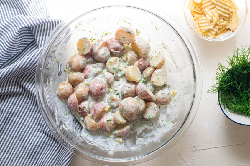 Creamy dill pickle potato salad being tossed in a large bowl