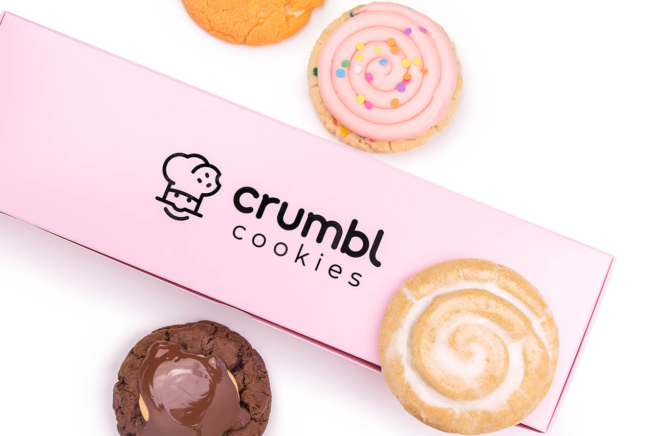 A box of Crumbl cookies with assorted cookies around it