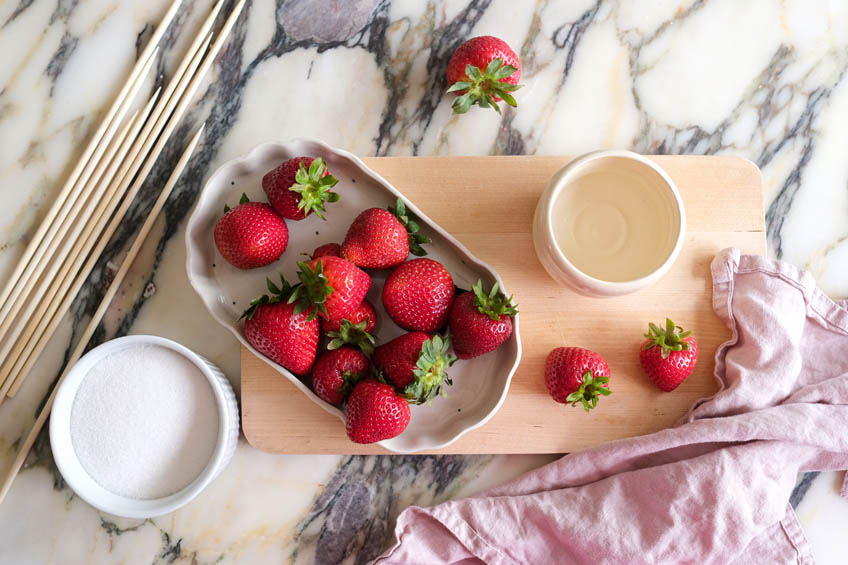 A flat lay of the ingredients for strawberry tanghulu including fresh strawberries, skewers and sugar