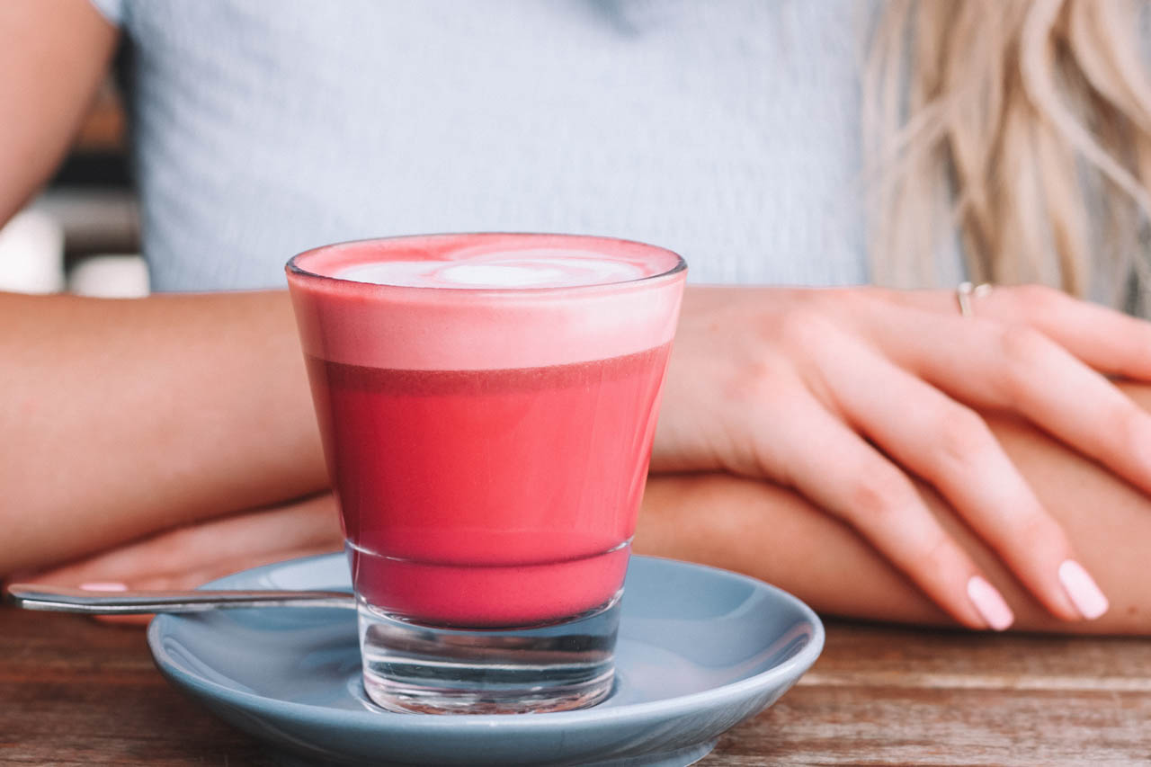 A beetroot latte on a table in front of a woman