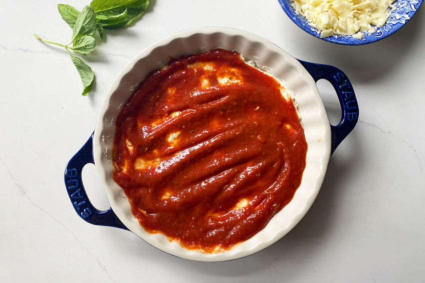 Cream cheese topped with tomato sauce in a pie dish