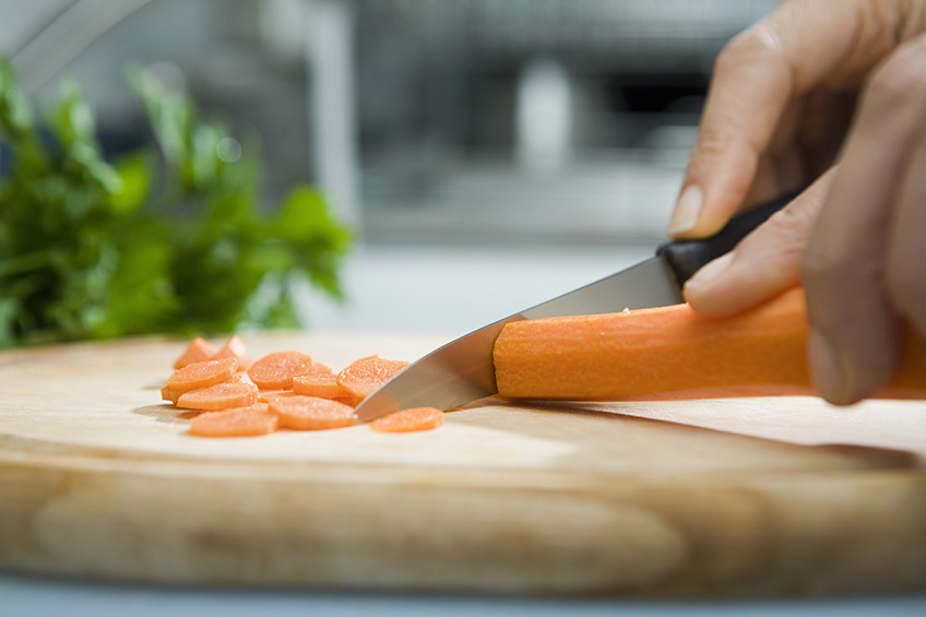 Close-up of hands chopping a carrot on a wooden cutting board.