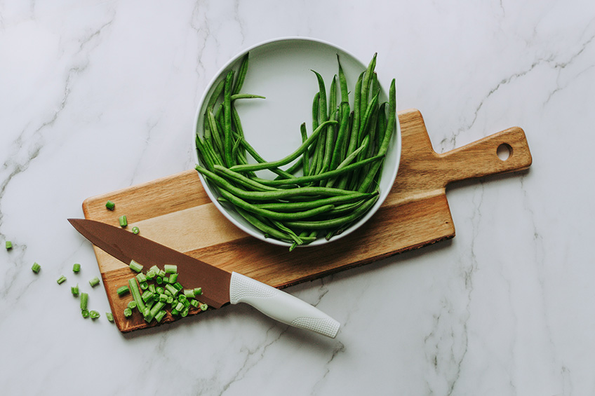 Green beans on a plate, with a few chopped pieces on a wooden cutting board.