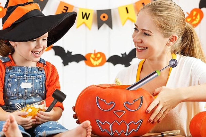 A child wearing a witch hat and an adult woman carving a pumpkin