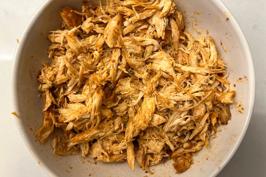 A white bowl with shredded spiced chicken