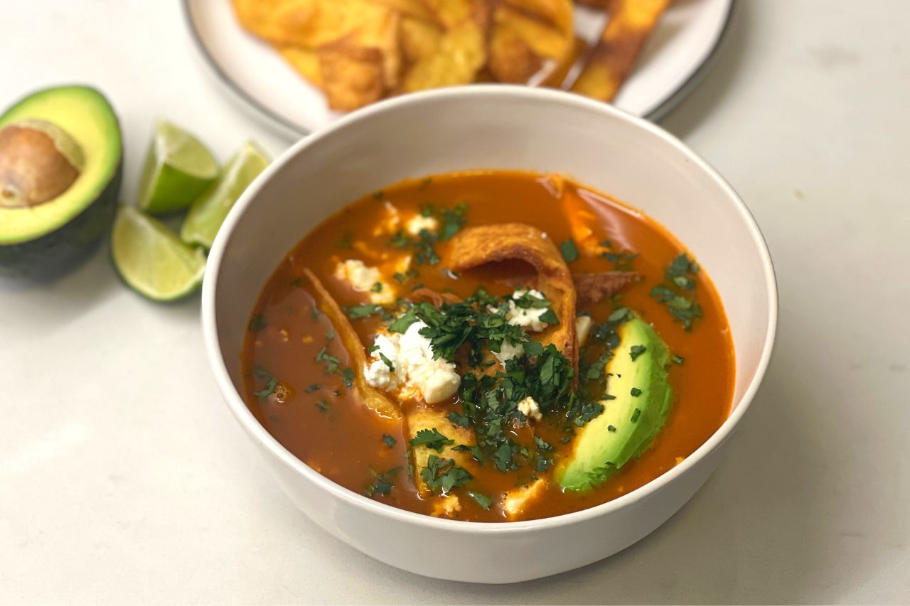 A shot of Sopa Azteca, a Mexican soup with fried tortilla chips, herbs, avocado
