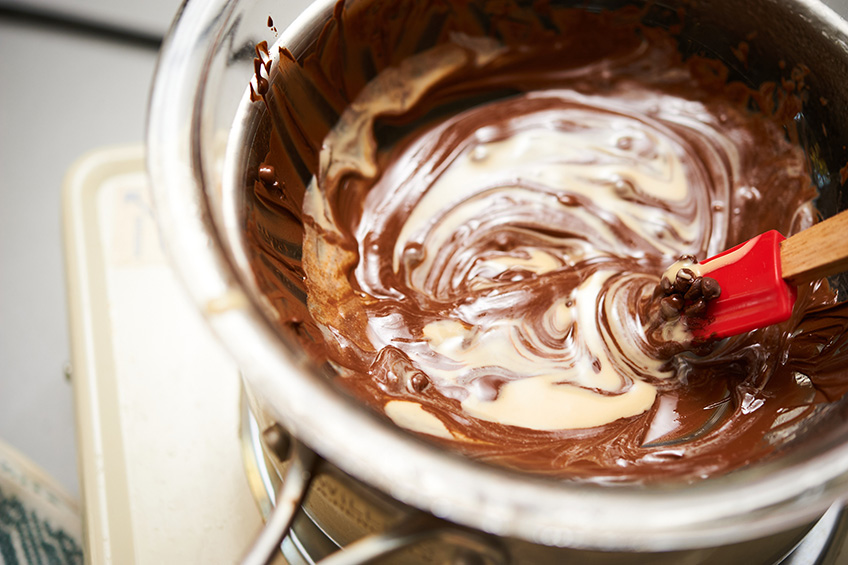 A spatula blending melted chocolate and tahini in a saucepan