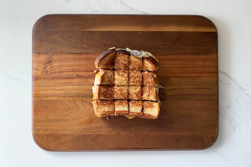 Grilled cheese on a wooden cutting board, cut into sixteen equal bite-sized squares