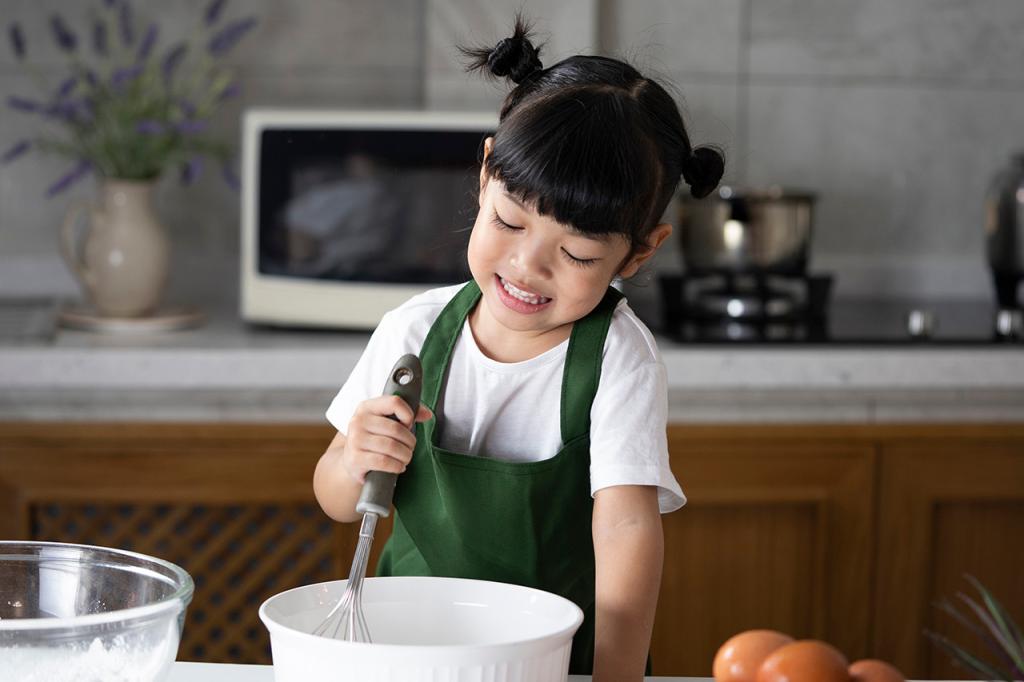 The child girl enjoys cooking in the kitchen. Happy Asian kid is preparing the dough, bake cookies in the kitchen.