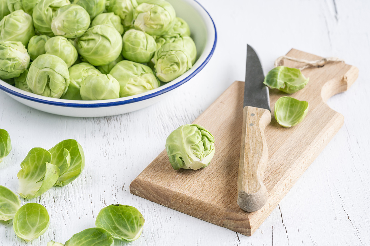 Brussel sprouts, removing outer leaves of fresh and ripe Brussel sprouts on wooden cutting board on white table or background. preparing raw green vegetables to cook