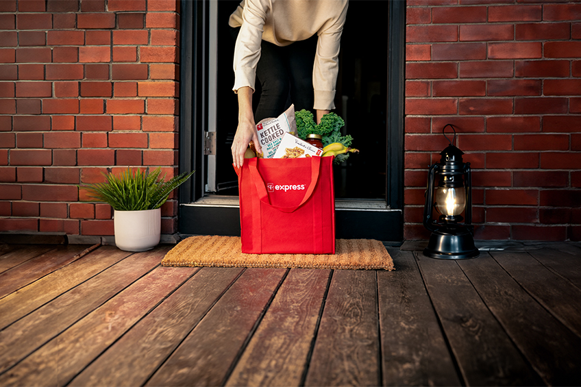 Image of a person picking up a red PC Express grocery delivery bag