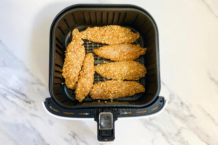 Raw chicken tenders coated with cooking spray in air fryer basket
