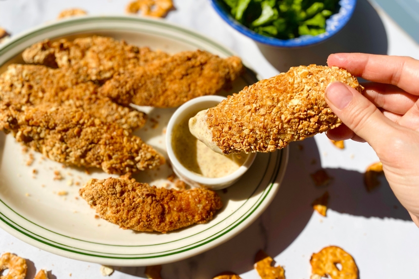 Pretzel-crusted chicken tenders being dipped into honey mustard dipping sauce