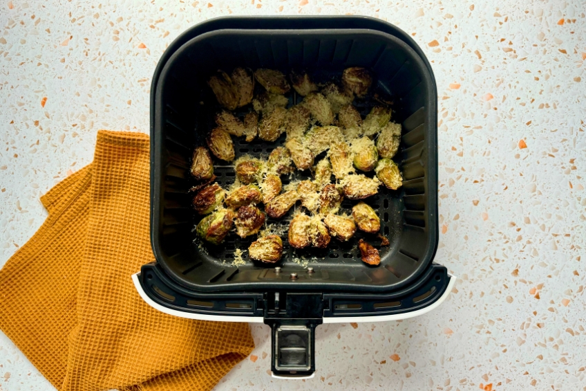 Roasted Brussels sprouts topped with Pecorino Romano in air fryer basket