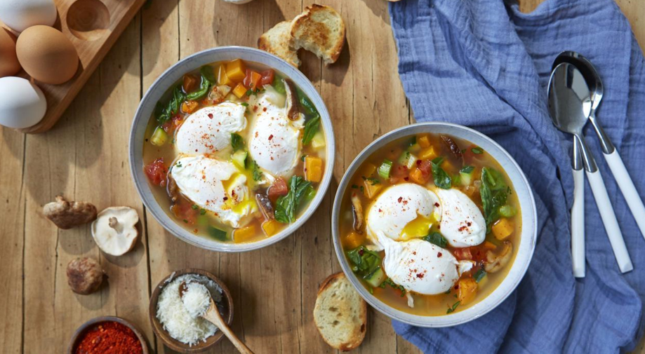 bowls of vegetable soup on a table with poached eggs on top