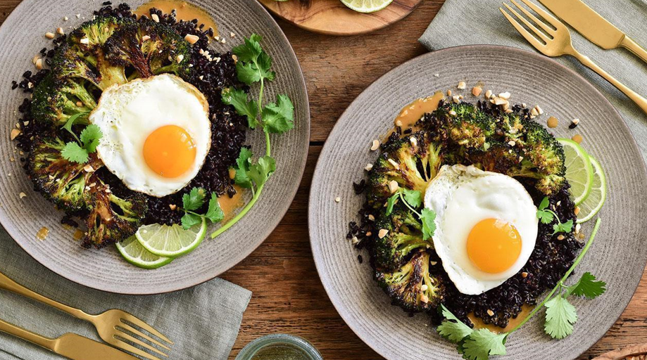 Stir-fried back rice with poached eggs presented on a table on grey plates