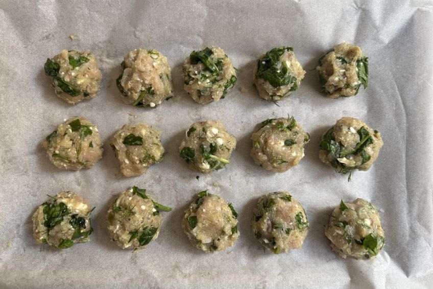 spinach and feta meatballs rolled out on a baking sheet